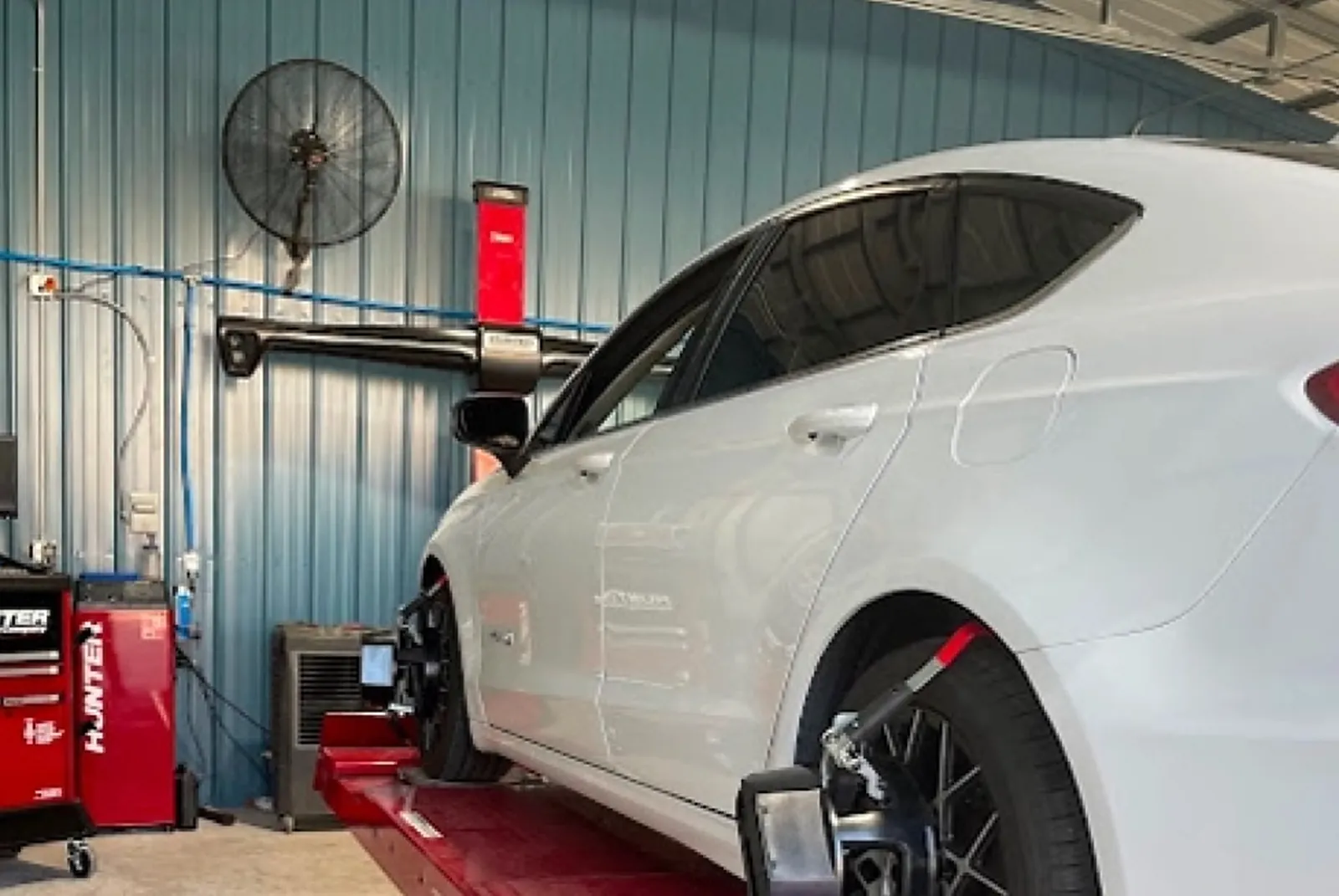 A white sedan on the red Hunter alignment lift inside the Paul's Auto & Collision shop