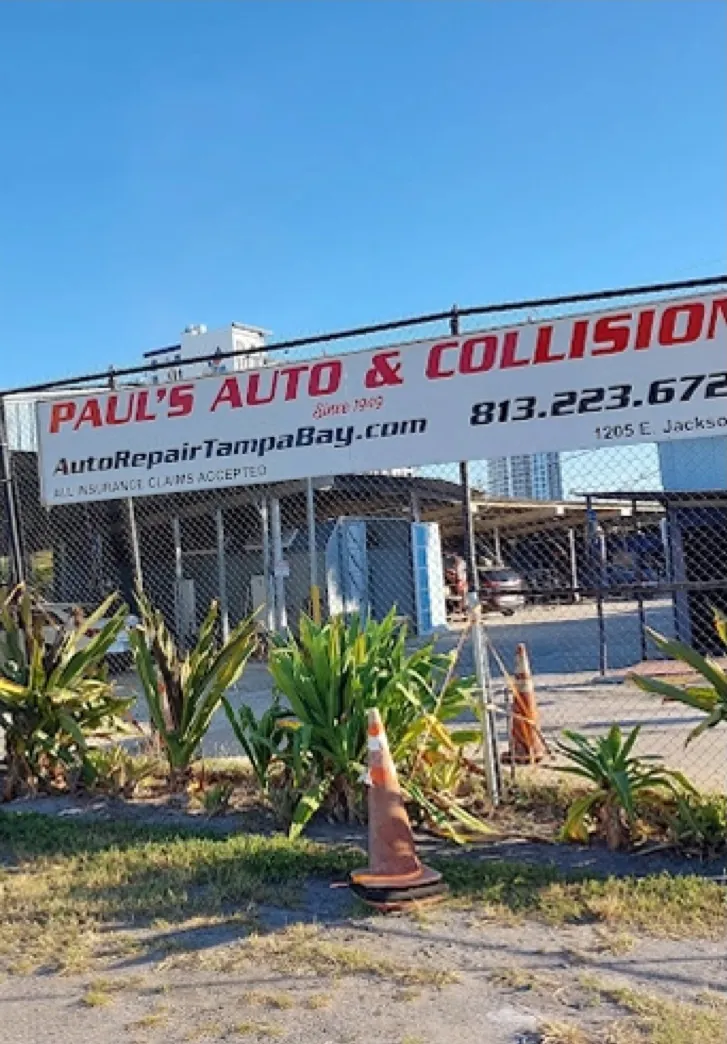 The Paul's Auto & Collision street sign, reading Since 1949, the web address and the shop phone number, on the fence at 1205 E Jackson St