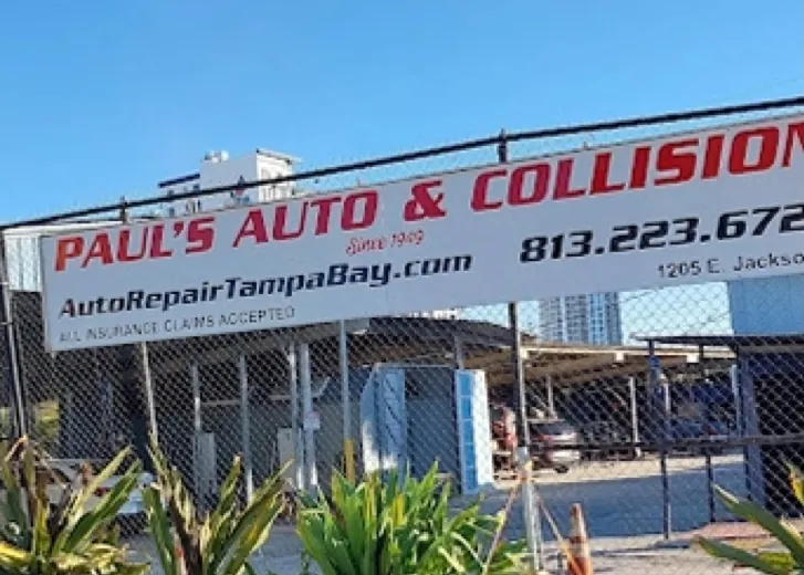 The Paul's Auto & Collision sign on the chain-link fence at 1205 E Jackson St, with the shop phone number
